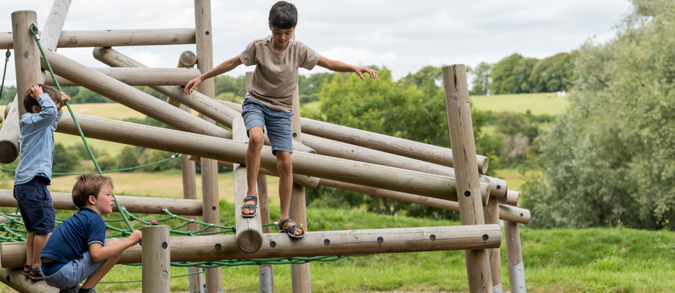 Three young boys playing on wooden play equipment outside